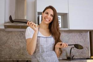 junge Frau in der Küche mit Schöpfkelle in der Hand lächelnd foto