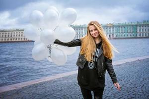 kaukasisches mädchen, das weiße luftballons hält, die am fluss auf dem damm stehen foto