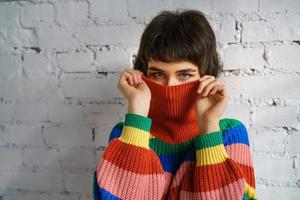 Porträt einer jungen Frau in einem bunten Pullover, die ihr Gesicht mit einem Pullover bedeckt. das Konzept der Schüchternheit foto