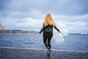 kaukasisches mädchen, das weiße luftballons hält, die am fluss auf dem damm stehen foto