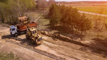 Bagger lädt den Sand in den LKW. Arbeiter machen den Weg. foto