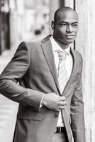 schöner schwarzer Mann, der Anzug im städtischen Hintergrund trägt foto