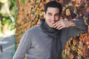 Mann trägt Winterkleidung lächelnd im Herbstlaub Hintergrund foto