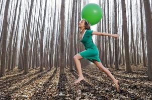 Schönes blondes Mädchen, grün gekleidet, springt mit einem Ballon in den Wald. foto