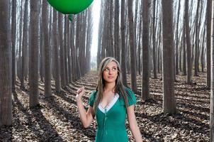 Schönes blondes Mädchen, grün gekleidet, im Wald stehend foto