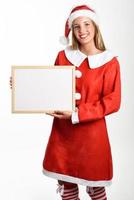 lächelnde blonde frau in weihnachtsmannkleidung mit weißer tafel foto
