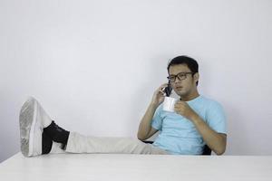 junger asiatischer mann schockiert, als er smartphone mit bein auf den tisch schaut foto