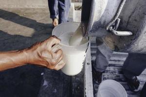 Landwirt gießt Rohmilch aus Milchviehbetrieb in Behälter zum Verkauf an Industrien oder Märkte foto