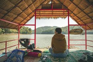 loei provinz, thailand dezember 2021 frau im gebiet des huai krathing reservoirs mit bambusfloßunterstand zum rafting und essen. schöne naturlandschaft des flusses und der berge mit blauem himmel foto