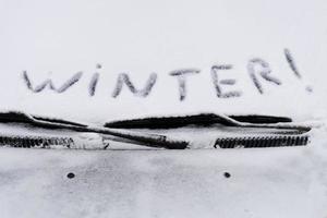 das Wort Winter steht auf dem Schnee, der die Windschutzscheibe des Autos bedeckt foto