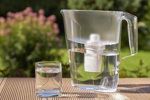 Wasserfilterkrug und ein sauberes Glas klares Wasser hautnah auf dem Hintergrund des Sommergartens foto