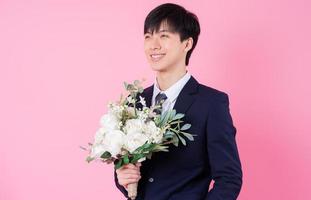 junger asiatischer bräutigam, der auf rosa hintergrund aufwirft foto