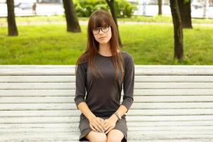 Porträt eines süßen Mädchens mit Brille, das auf einer Bank auf der Straße im Park sitzt foto