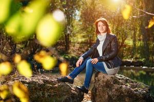 junge Frau auf einem Felsen am Teich im Herbstpark foto