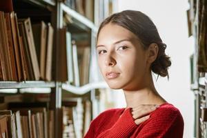 Porträt eines Mädchens, das in der Bibliothek vor dem Hintergrund von Büchern steht foto