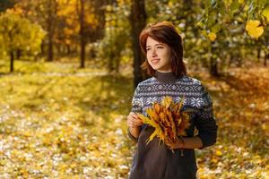 Fröhliche junge Frau im Herbstpark, die an einem sonnigen Tag lächelt foto