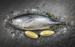 frischer Fisch mit Kräutergewürzen Rosmarin und Zitrone - roher Fisch Meeresfrüchte auf schwarzem Hintergrund Draufsicht, Longtail-Thunfisch, östlicher kleiner Thunfisch? foto