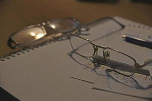 notizbuch und brille auf dem tisch am abend foto