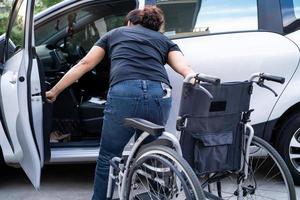 asiatische Frau, die den Rollstuhl in ihr Auto faltet und anhebt. Konzept der Barrierefreiheit. foto