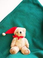 Spielzeug-Eisbär in einem roten Weihnachtsmann-Hut mit Schleife auf grünem Hintergrund. Weihnachtsgrußkarte. tier, flatlay, kopierraum, platz für text foto