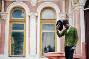 Modeporträt eines schwarzen Afroamerikaners auf grüner Samtjacke Bleiben Sie auf der Treppe und tragen Sie seinen schwarzen Hut im Hintergrund Altes Herrenhaus. foto