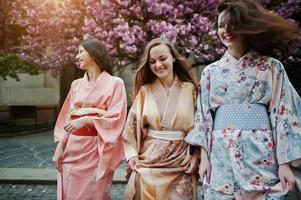 drei europäische mädchen, die traditionellen japanischen kimonohintergrund tragen, blühen rosa sakura-baum foto