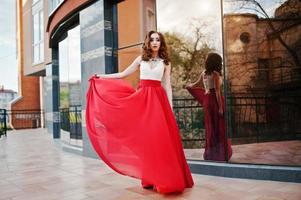 Porträt des modischen Mädchens im roten Abendkleid stellte Hintergrundspiegelfenster des modernen Gebäudes