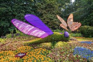 Schmetterlings- und Libellenfigur, die in einer farbenfrohen Blumenausstellung im Garten steht foto