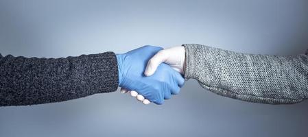 Händeschütteln in medizinischen Handschuhen auf grauem Hintergrund. das Konzept eines sicheren Händedrucks. foto