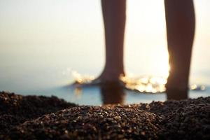 Kieselsteine an der Küste vor dem Hintergrund von Frauenfüßen in einer Unschärfe. Mädchenfüße sind verschwommen und unscharf, die Sonnenstrahlen betonen die Beine. foto