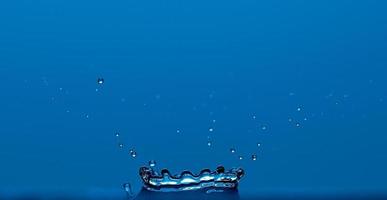 Reines klares Wasser spritzt wie eine Krone isoliert auf blauem Hintergrund. foto
