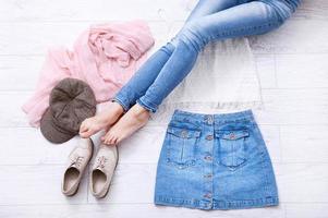 Stilvolles Sommeroutfit mit verschiedenen Accessoires und weiblichen Beinen in Jeans auf weißem Holzboden. draufsicht und kopierraum. foto