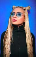 blonde Frau mit Piercing und afrikanischen Zöpfen in blauer Sonnenbrille foto