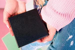 Frauenhände mit rosafarbener Maniküre, die eine schwarze Geschenkbox hält foto