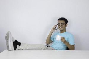 junger asiatischer mann fühlt sich glücklich und lächelt, wenn er mit dem bein auf dem tisch am telefon spricht. foto