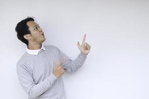 junger asiatischer mann mit weißem hemd ist überrascht und schreit wow, indem er mit dem finger nach rechts zeigt, isoliert auf grauem hintergrund mit kopierraum für ihren text. foto