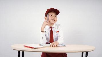 asiatische Mädchen der Grundschule, die an eine Idee denken, isoliert auf einem weißen Hintergrund zu schreiben foto