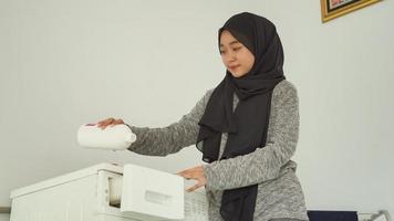 Schöne Frau im Hijab gießt Waschmittel für ihre Wäsche zu Hause foto