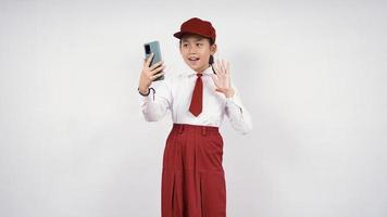 Grundschule asiatisches Mädchen winkt auf ihrem Telefonbildschirm isoliert auf weißem Hintergrund foto