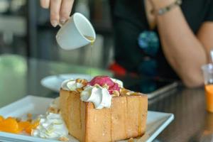 Gießen Sie Honig auf Honigtoast mit rotem hausgemachtem Eis und Schlagsahne, servieren Sie ihn mit Orange im Café und Restaurant. foto