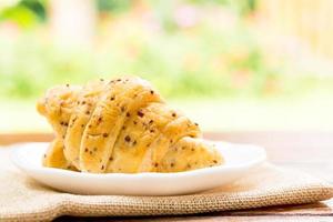 Frühstückskonzept. Croissants mit Perilla-Samen auf weißem Teller und weiße Tasse schwarzen Kaffee auf Holztisch mit grünem Bokeh-Hintergrund. foto