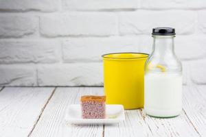 gelbe Tasse und eine Flasche frische Milch, serviert mit einem quadratischen Stück Süßkartoffelkuchen auf einem weißen Teller in der Küche. Bäckerei- und Getränkekonzept. foto