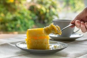 Eatting Slice Orangenkuchen mit Metallgabel serviert auf weißem Teller auf Tischdecken in Kaffeezeiten mit grünem Natur-Bokeh-hellem Hintergrund. foto