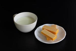 Seitenansicht vier Waffeln in weißer Platte mit Tasse Milch auf schwarzem Hintergrund mit Kopierraum. foto