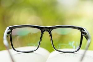 Buch und Brille auf Holztisch mit abstraktem grünem Naturunschärfehintergrund. Lese- und Bildungskonzept foto