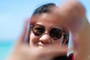 Porträt einer asiatischen reifen erwachsenen Frau, die eine Sonnenbrille mit Meereshintergrund trägt foto