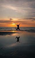 Silhouette einer Frau, die bei Sonnenuntergang am Strand springt foto