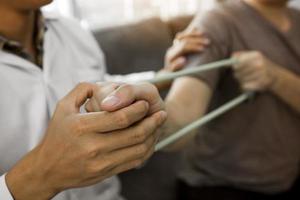 Nahaufnahme eines Handpatienten, der Dehnübungen mit einem flexiblen Übungsband und einer Hand eines Physiotherapeuten durchführt, um im Klinikraum zu helfen. foto