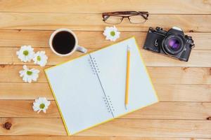 auf hölzernem Hintergrund Notebook-Bleistift, Kaffee und Blumen. foto