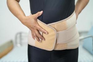 asiatische Patientin mit Rückenschmerzen-Unterstützungsgurt für orthopädische Lendenwirbelsäule. foto